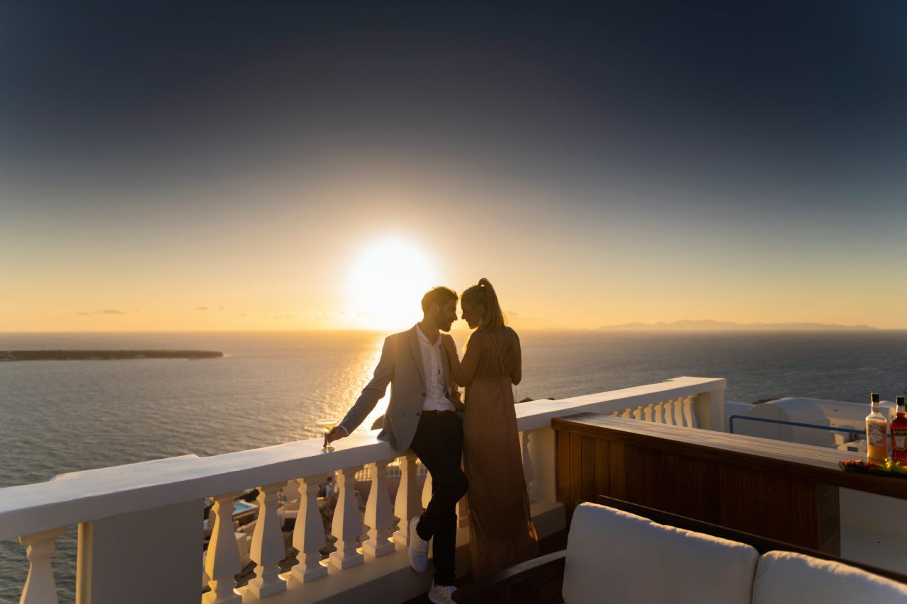 Paar, das den atemberaubenden Sonnenuntergang von der Terrasse des Oia Mansion Beobachtet – Luxury 4-Schlafzimmer-Villa zur Miete auf Santorin